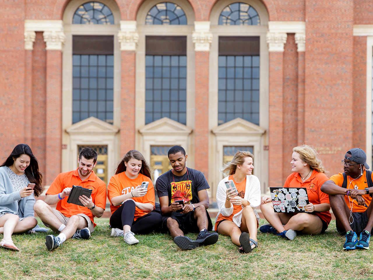 7 people sit in front Edmon Low Library looking at their devices