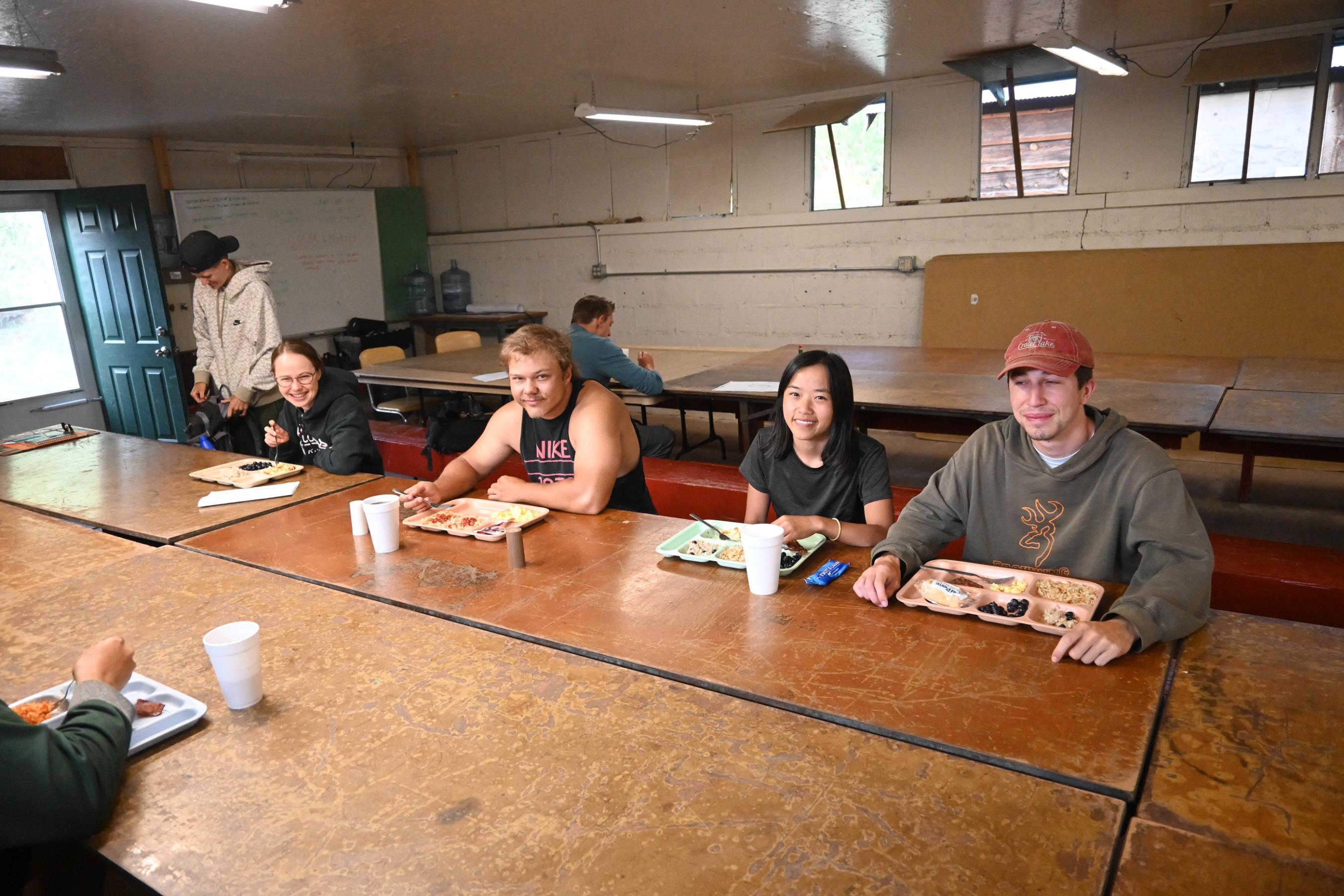 Six students sitting down to eat a meal in the dining hall. Six students sitting down to eat a meal in the dining hall.