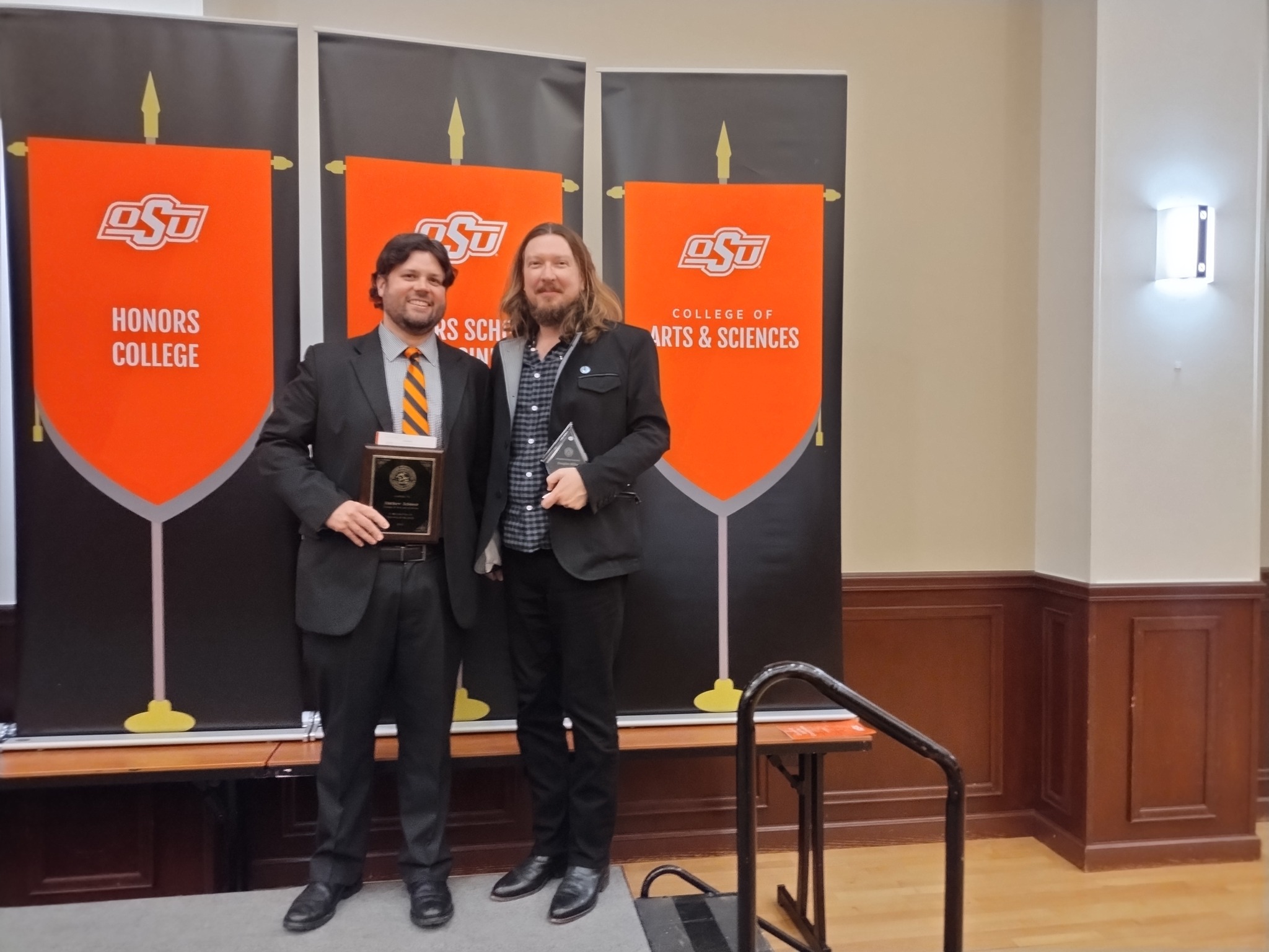 Schauer and Miller Two men standing with awards against an orange and black background