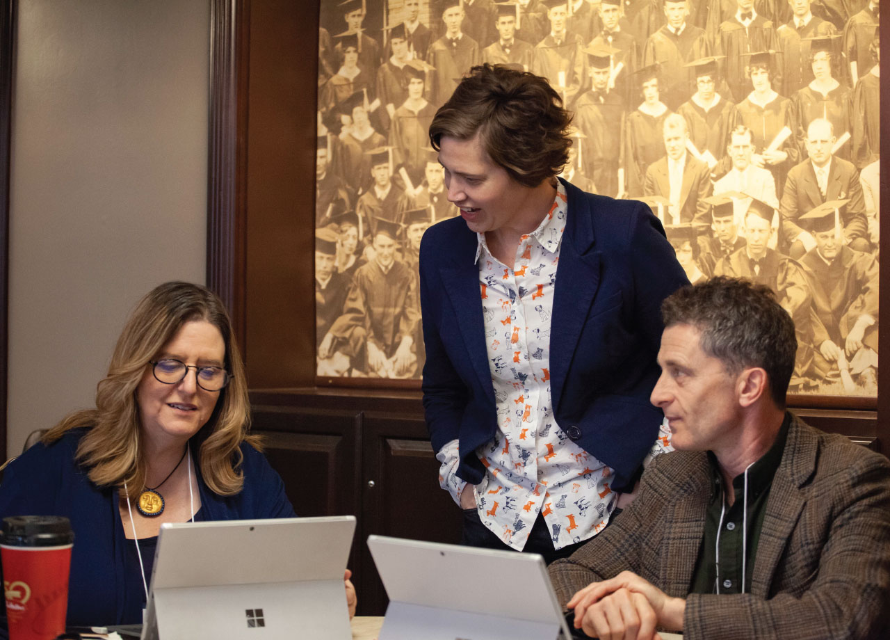 Two women and one man at a table looking at iPads and conversing