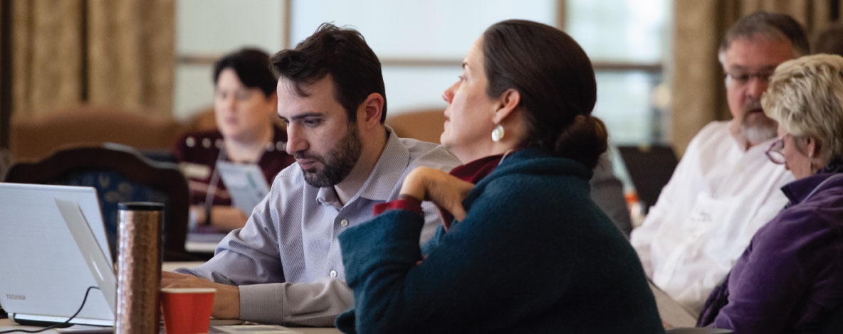 Digital Humanities, 5 people seated at tables working at laptops on large wooden desks