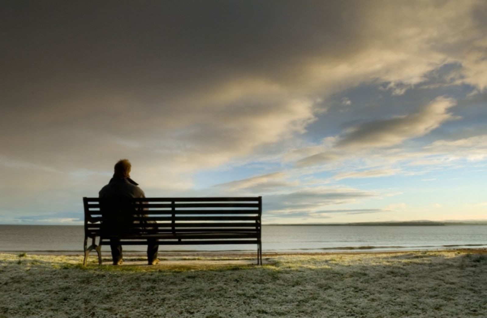 Bench with a man sitting on it facing the setting sun Bench with a man sitting on it facing the setting sun