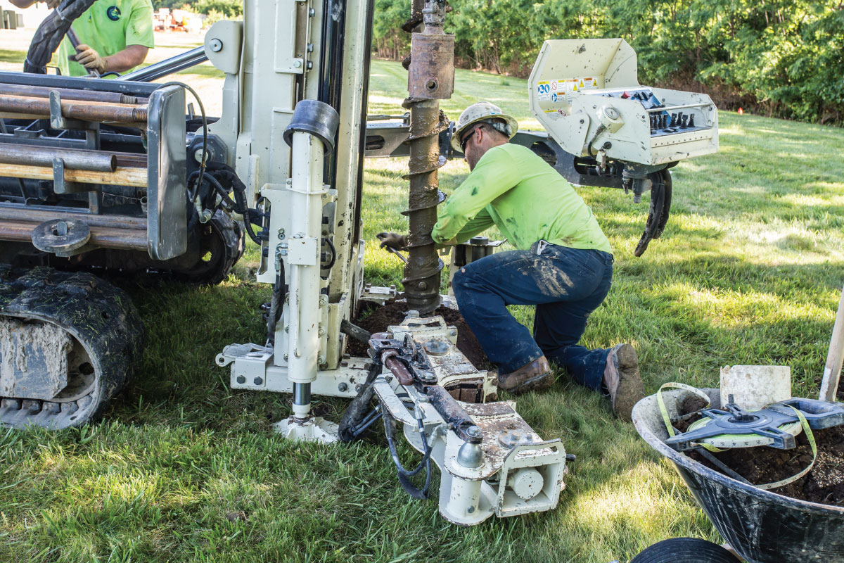A man in a hard hat down on one knee working on a large drill used for major drilling jobs. A man in a hard hat down on one knee working on a large drill used for major drilling jobs.