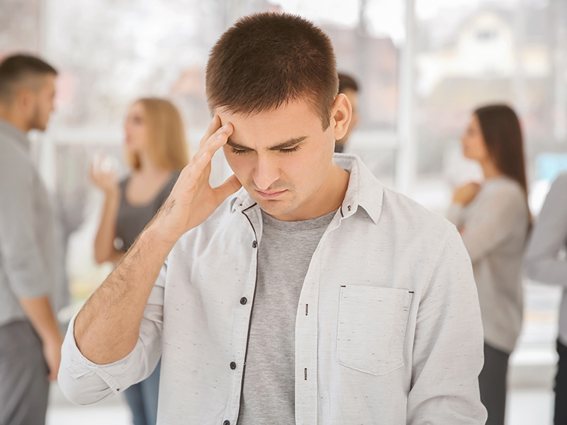 social anxiety man standing away from crowd massaging his forehead