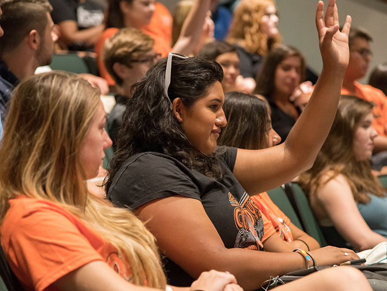 increase_enrollment.jpg Two females sitting in stands with and one has her hand raised.