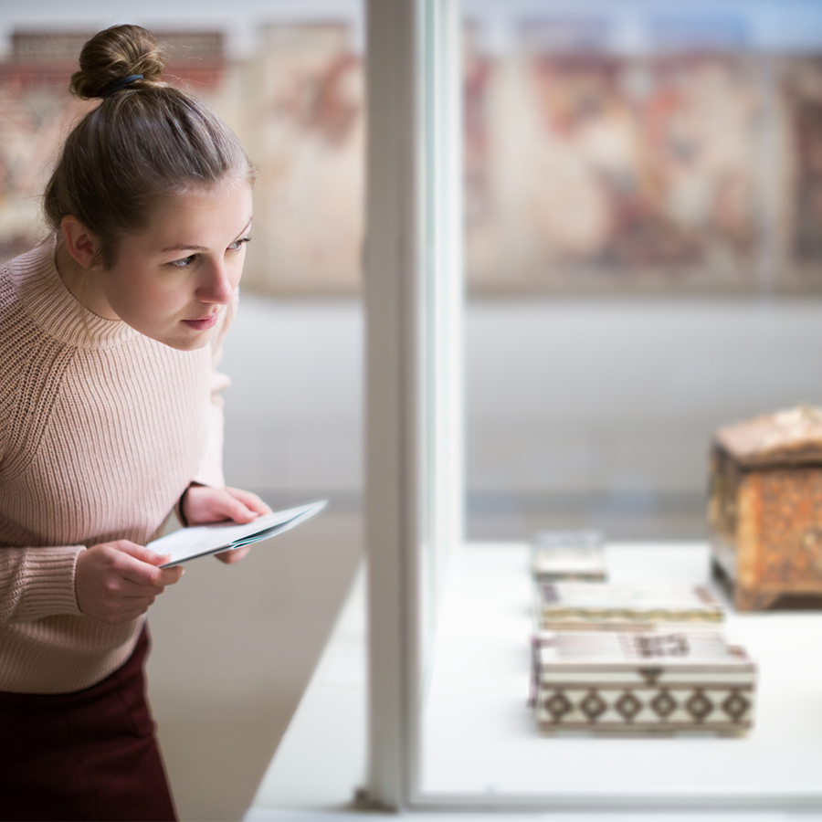 Woman looking at historical art objects behind glass