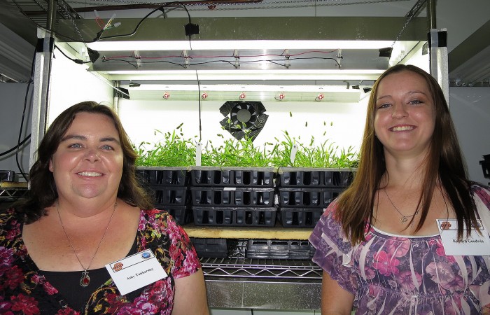 Amy and Kaytlyn stand before an experimental enclosure in the growth chamber.
