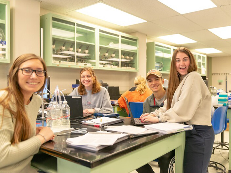 Students gathered around a table working in the lab. Students gathered around a table working in the lab.