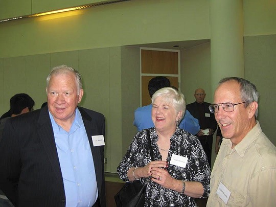 hree individuals with name tags in a social setting, with other people and a column visible in the background hree individuals with name tags in a social setting, with other people and a column visible in the background