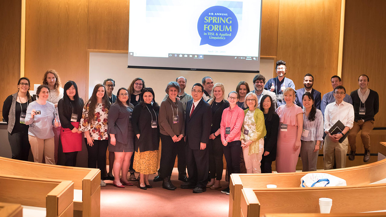 A large group of people smile at the front of a lecture hall. A large group of people smile at the front of a lecture hall.
