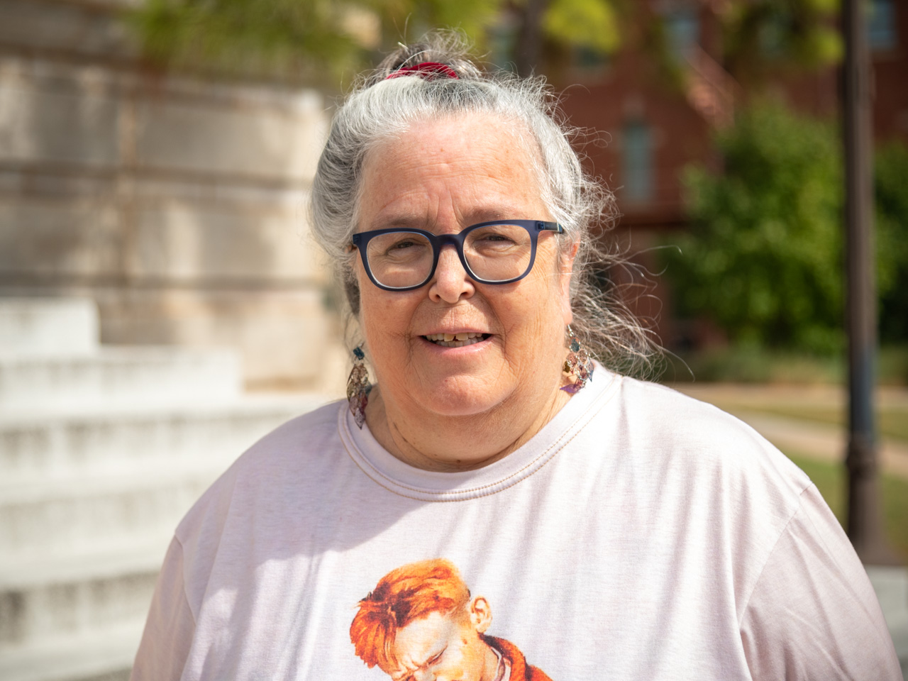 A woman with gray hair in a bun and a light pink shirt smiles