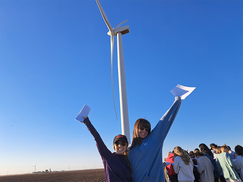 Female students on a field trip in front of a wind tower in the Gloss Mountains