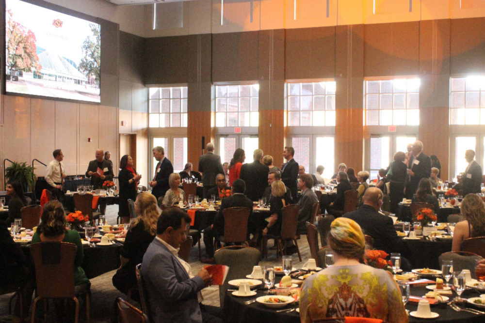 The banquet hall full of people standing and visiting before the meal.
