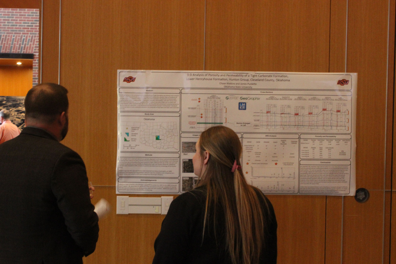 A female student showing a male alumni member her presentation poster.