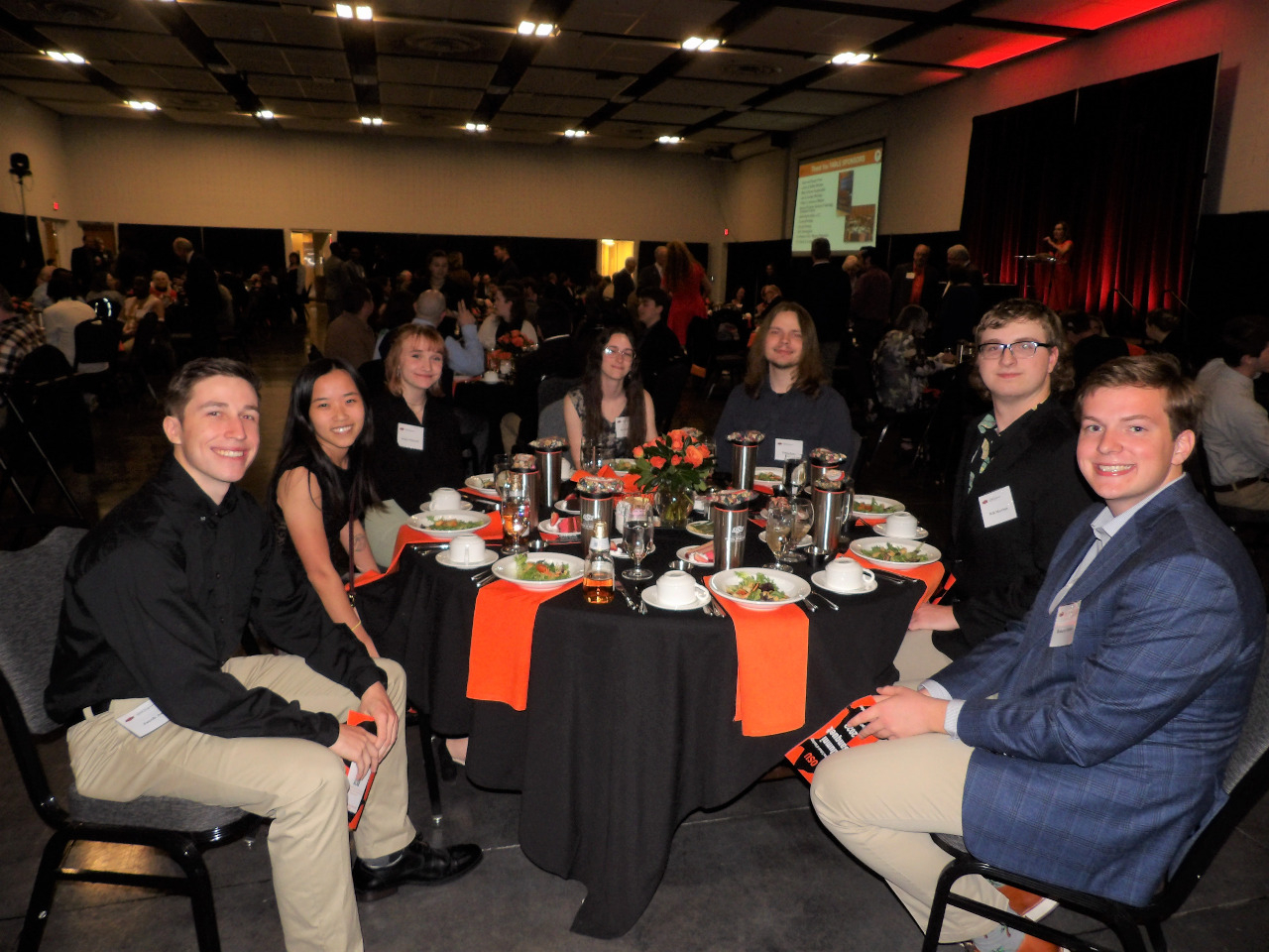 Four male and three female students sitting down enjoying the banquet dinner.