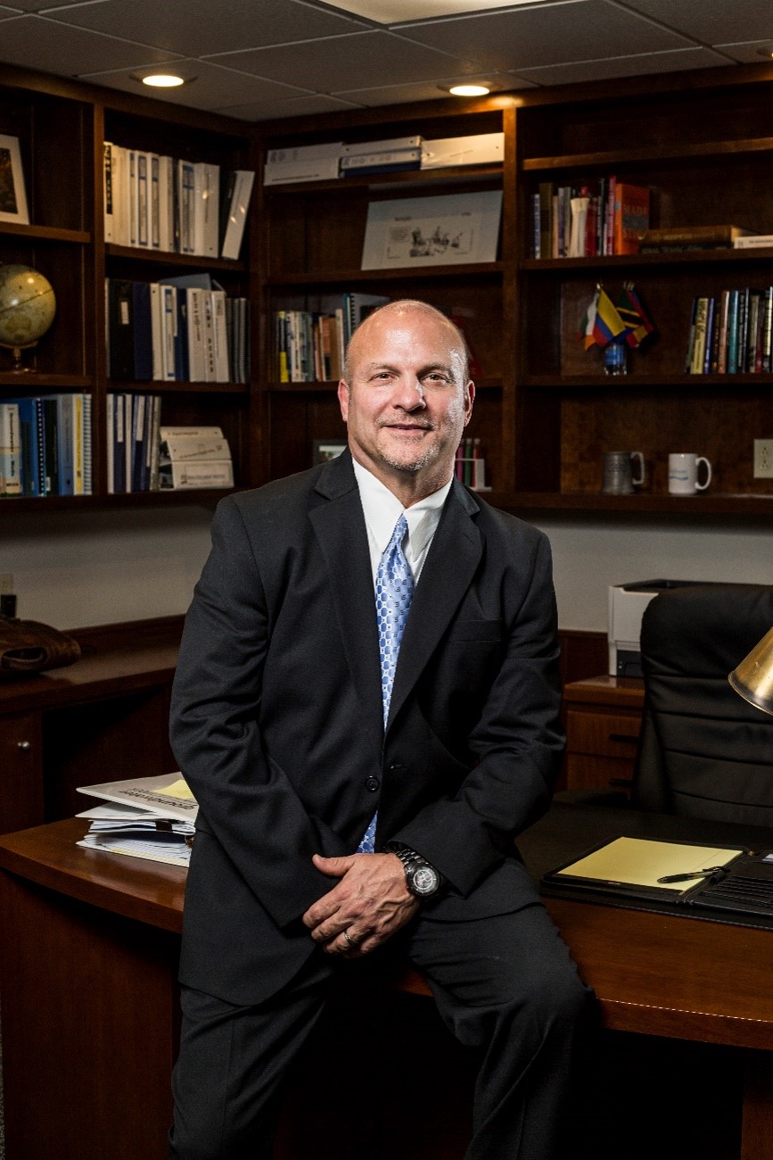 Mr. Terry Morse sitting on a desk in his office posing for a photo.