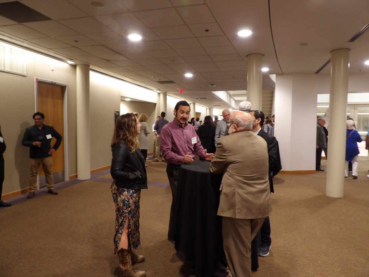Three males and one female visiting in banquet hall before banquet begins.