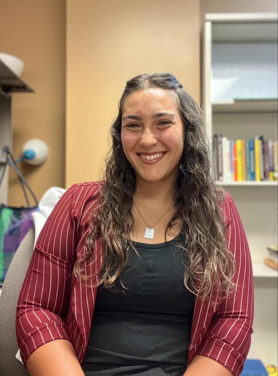 A woman with long brown curly hair weaing a burgundy shirt with buttons.