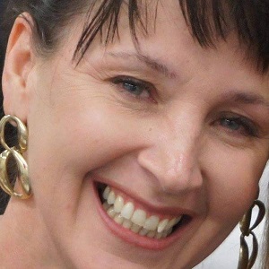 A close shot of a woman smiling with gold dangle earrings and brown fringe bangs.