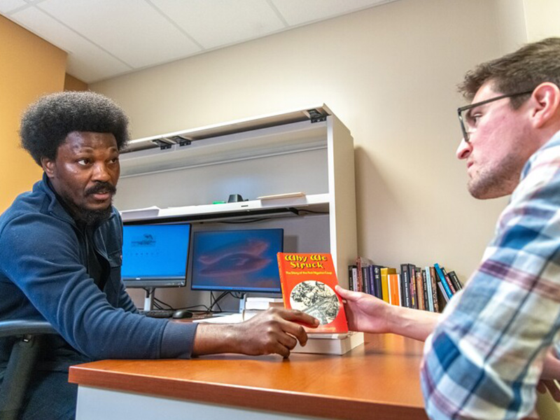 Faculty member introducing a book to students sitting at a table.