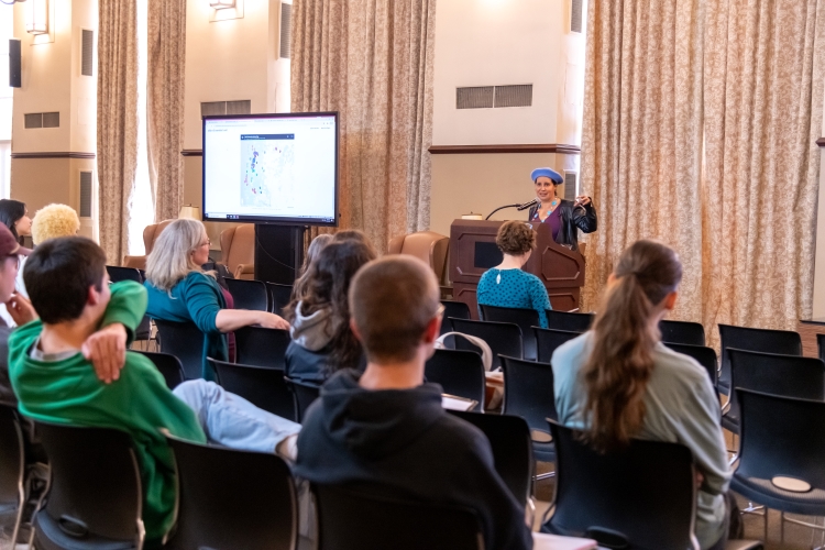 Dr. Reyes-Santos speaking at a podium to a seated audience. Dr. Reyes-Santos speaking at a podium to a seated audience.