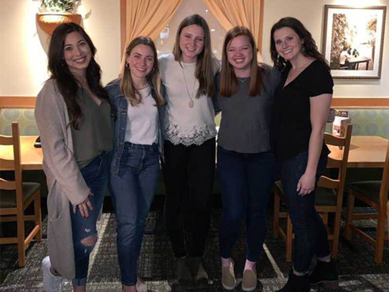 Five female students with arms around each other smiling at camera