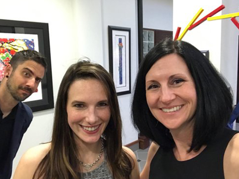 Two females wtih a male photo bombing behind smiling at camera