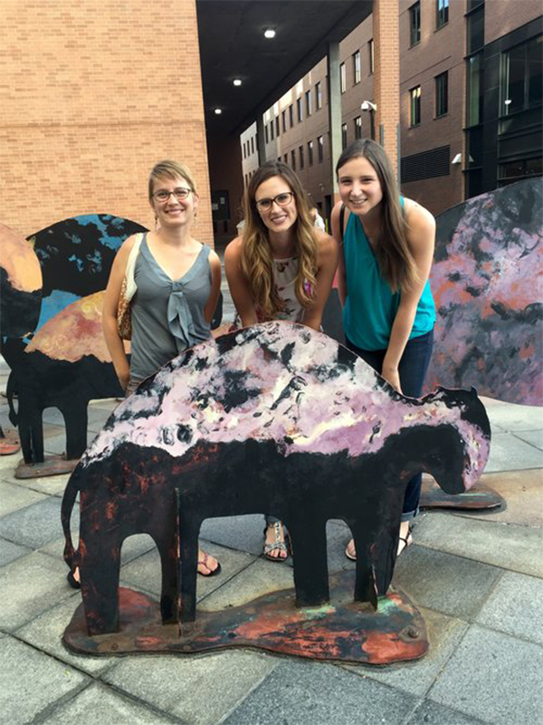 Three female students behind a metal mini buffalo smiling at camera