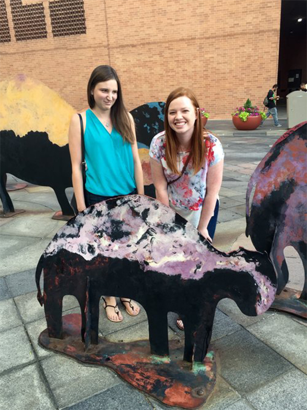 Two female students behind a metal mini buffalo smiling at camera