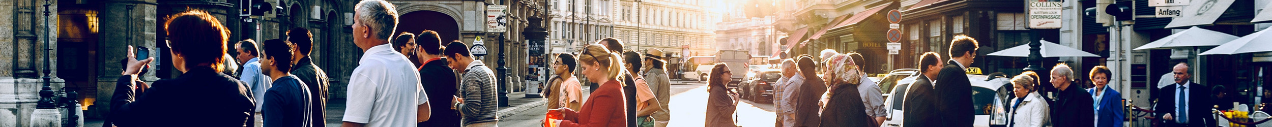 Crowded city street during daytime, with dozens of pedestrians walking in various directions past storefronts.