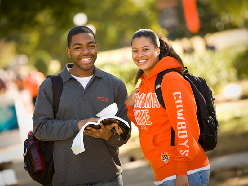 A boy and a girl students, both smiling, holding books in their hands, standing together.